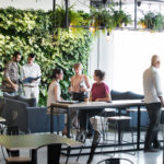 Espace de travail commun dynamique avec plusieurs groupes de personnes en réunion autour de tables et canapés.