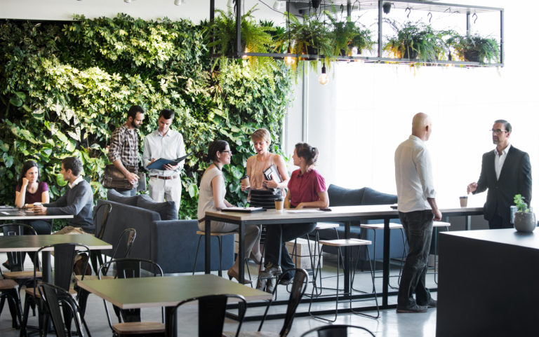 Espace de travail commun dynamique avec plusieurs groupes de personnes en réunion autour de tables et canapés.